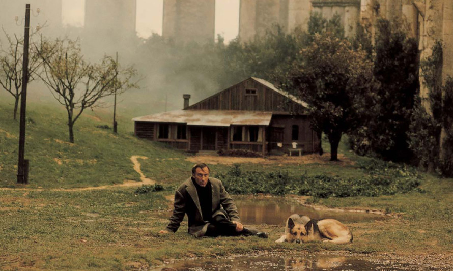 Imagem do filme "Nostalgia" - um homem e um cão sentados na relva em frente a uma casa