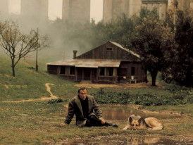 Imagem do filme "Nostalgia" - um homem e um cão sentados na relva em frente a uma casa